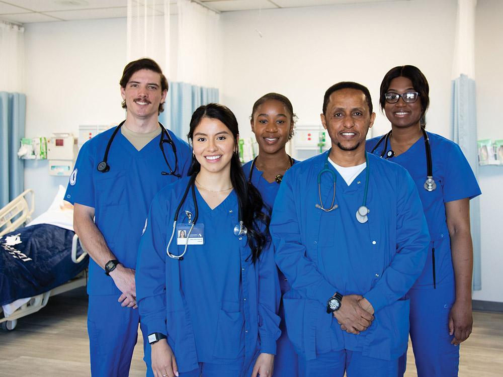 Five students in medical scrubs standing in 护理 lab