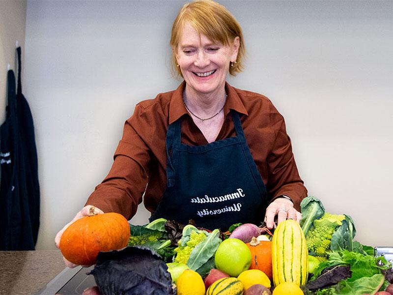 Woman in apron behind pile of fresh fruit and vegetables